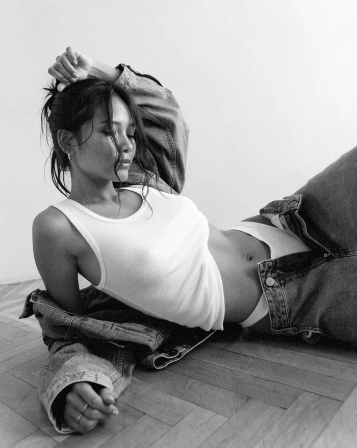 Black-and-white photograph of Ellequa reclining on a wooden floor in denim.